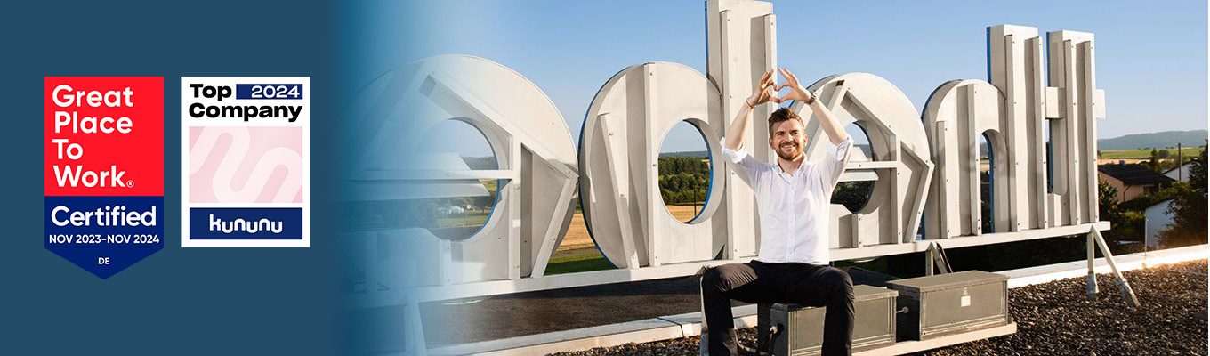 Theben – Ausgezeichnet als attraktiver Arbeitgeber in der Region Theben-Geschäftsführer Paul Sebastian Schwenk zeigt mit Händen ein Herz vor dem Theben-Firmenlogo auf dem Büro-Dach, daneben Siegel „Great Place to Work- Zertifiziert“ und „Kununu Top Company 2024"